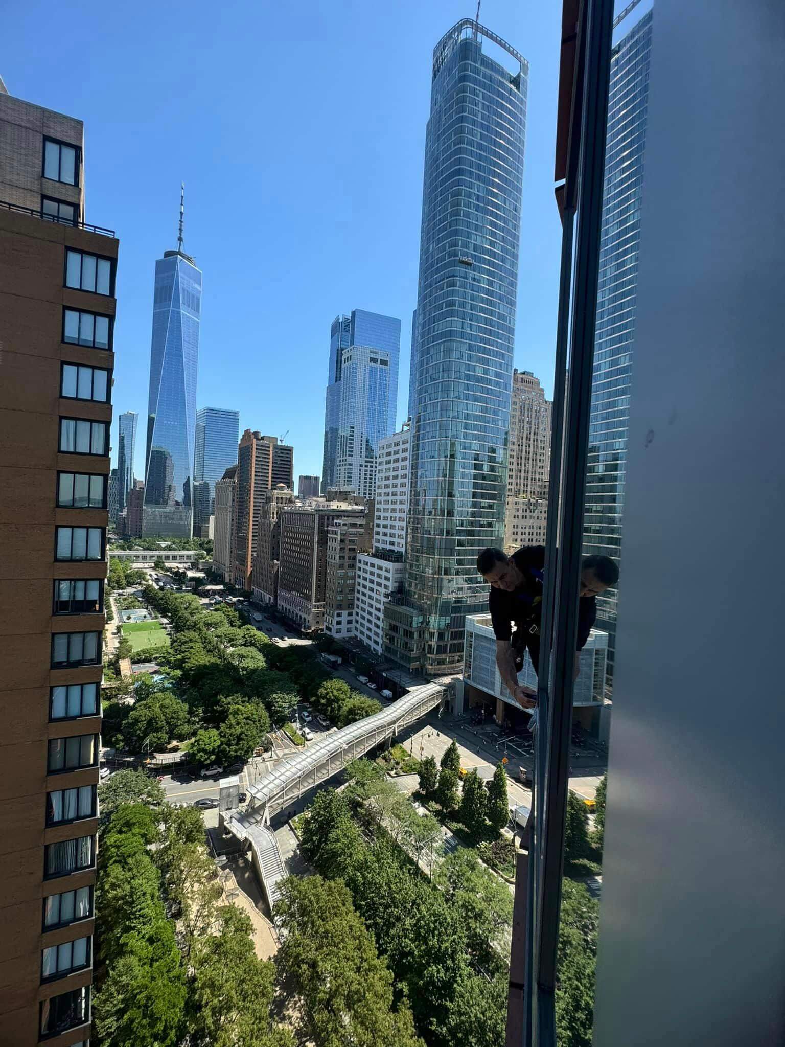 Technician cleaning exterior high rise window overlooking NYC